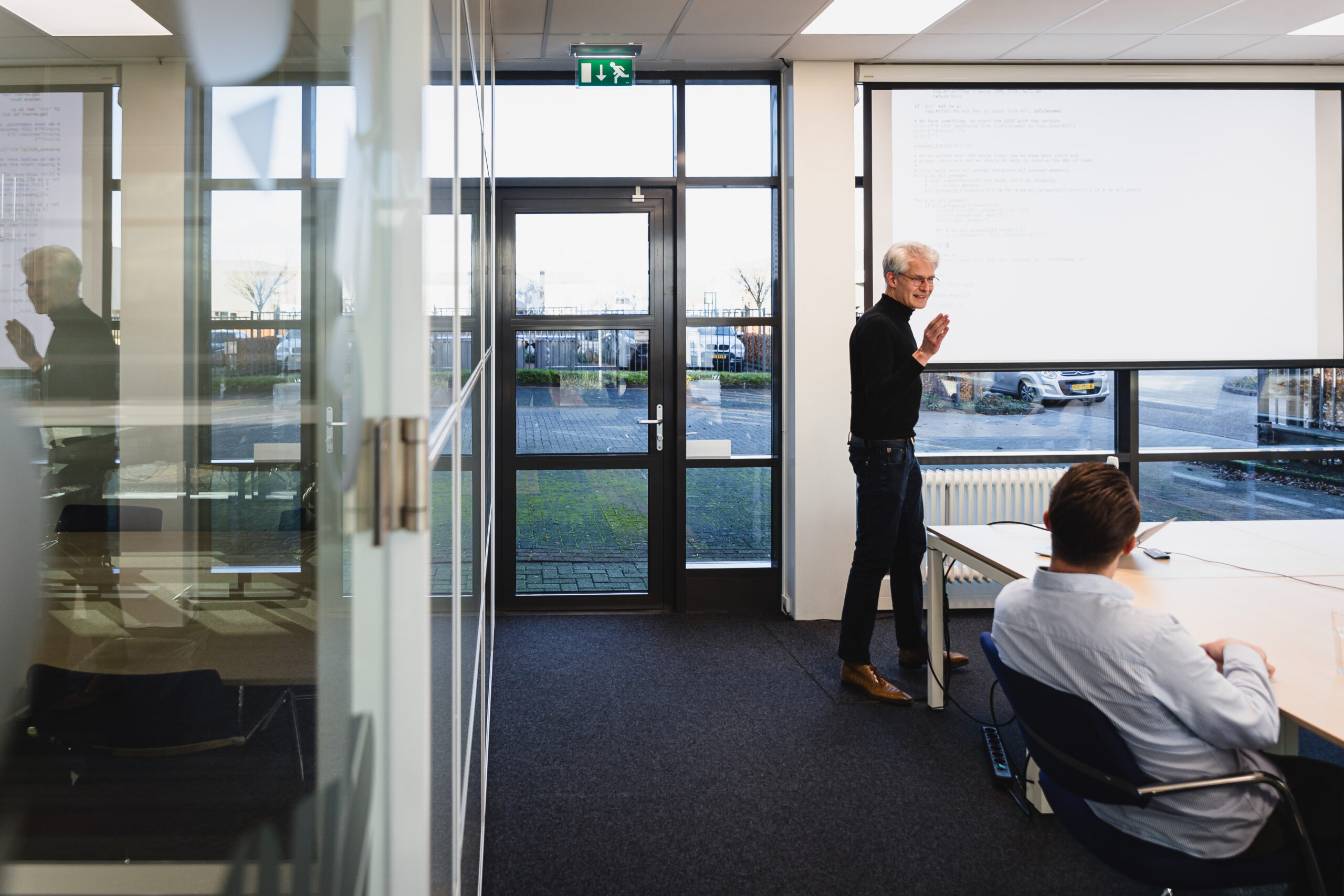 Two people in a meeting room. One person in front of a screen presenting.