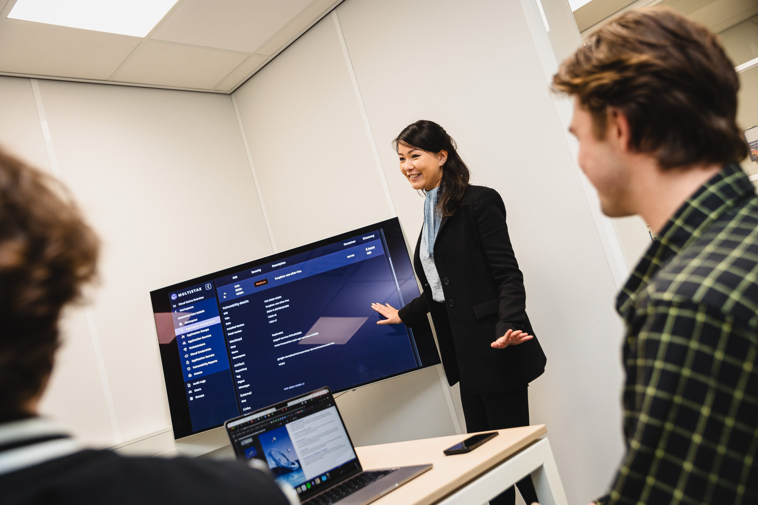 Three people in a meeting room. One person in front of a screen presenting.