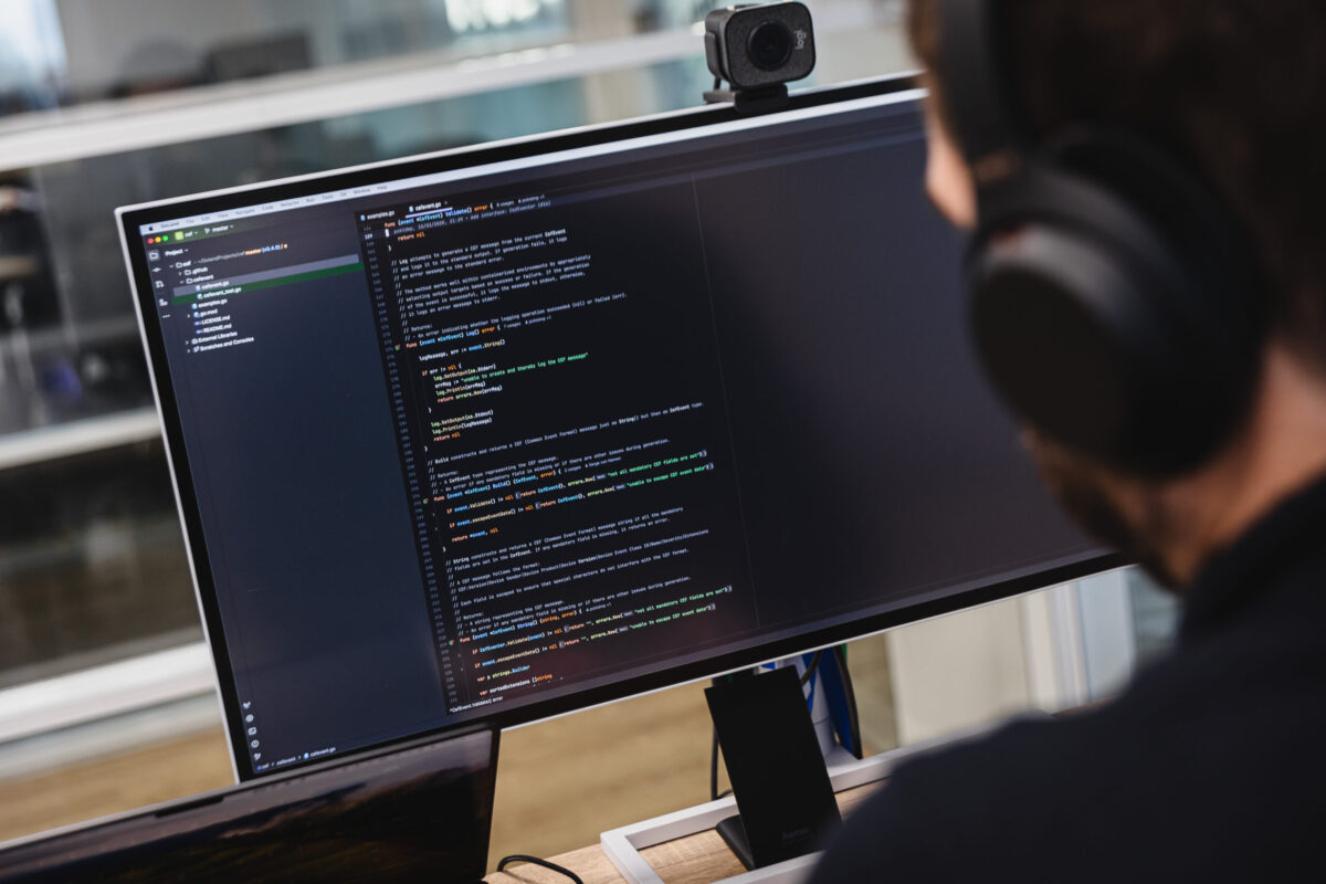 A person with headphones in front of a screen with lines of code. Seen from behind.