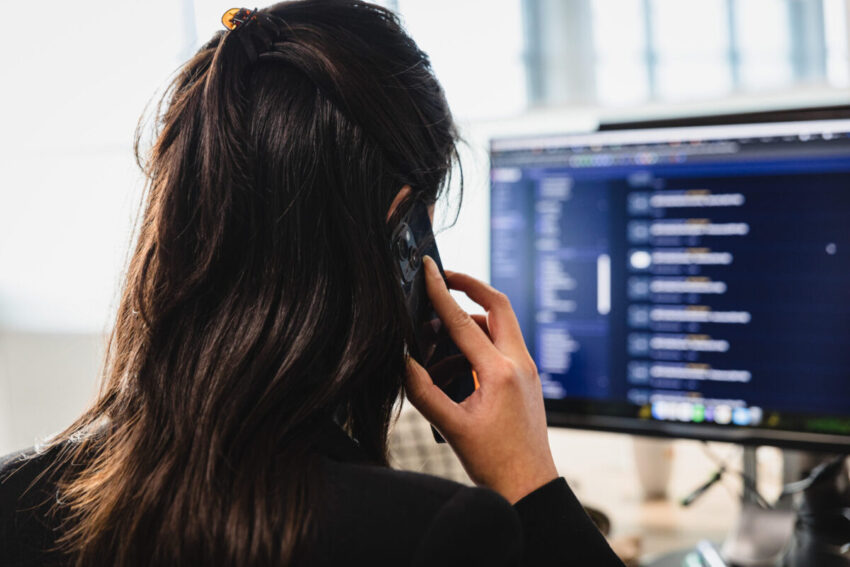 A women seen from the back who is on the phone behind a screen with lines of code.