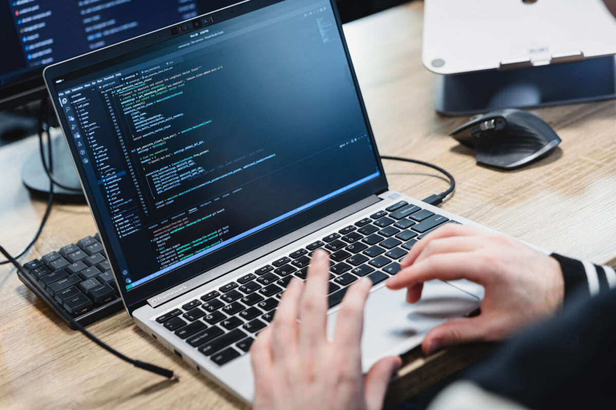 A laptop screen with lines of codes and the hands of a person.