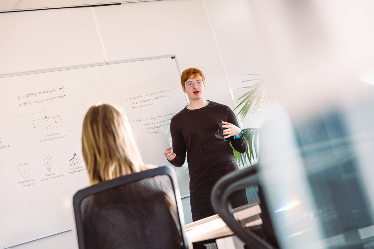 Two people in a meeting room, one in front of a whiteboard.