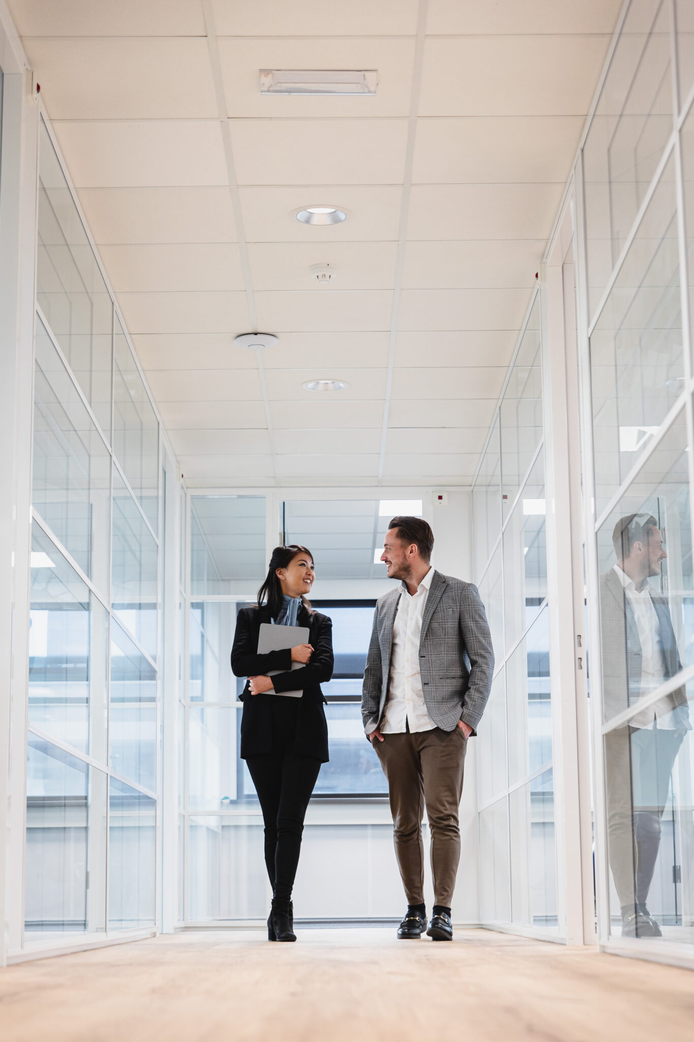 Two people walking down an office hallway. One holding a laptop.