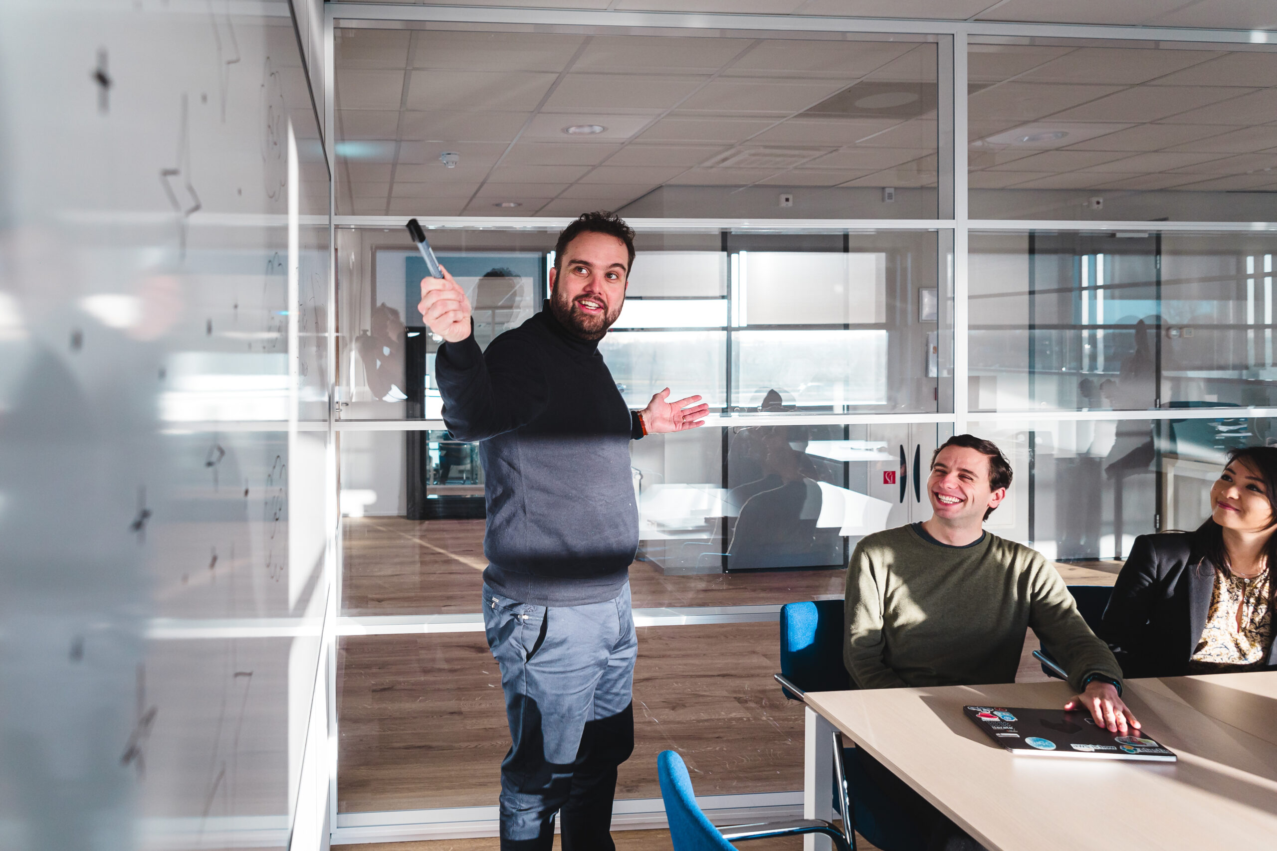 Three people in a meeting room, one standing in front of a whiteboard.