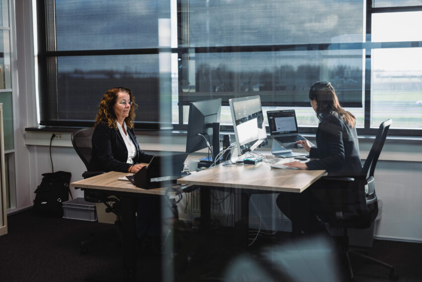 Two people sitting behind their desk, working on laptops.