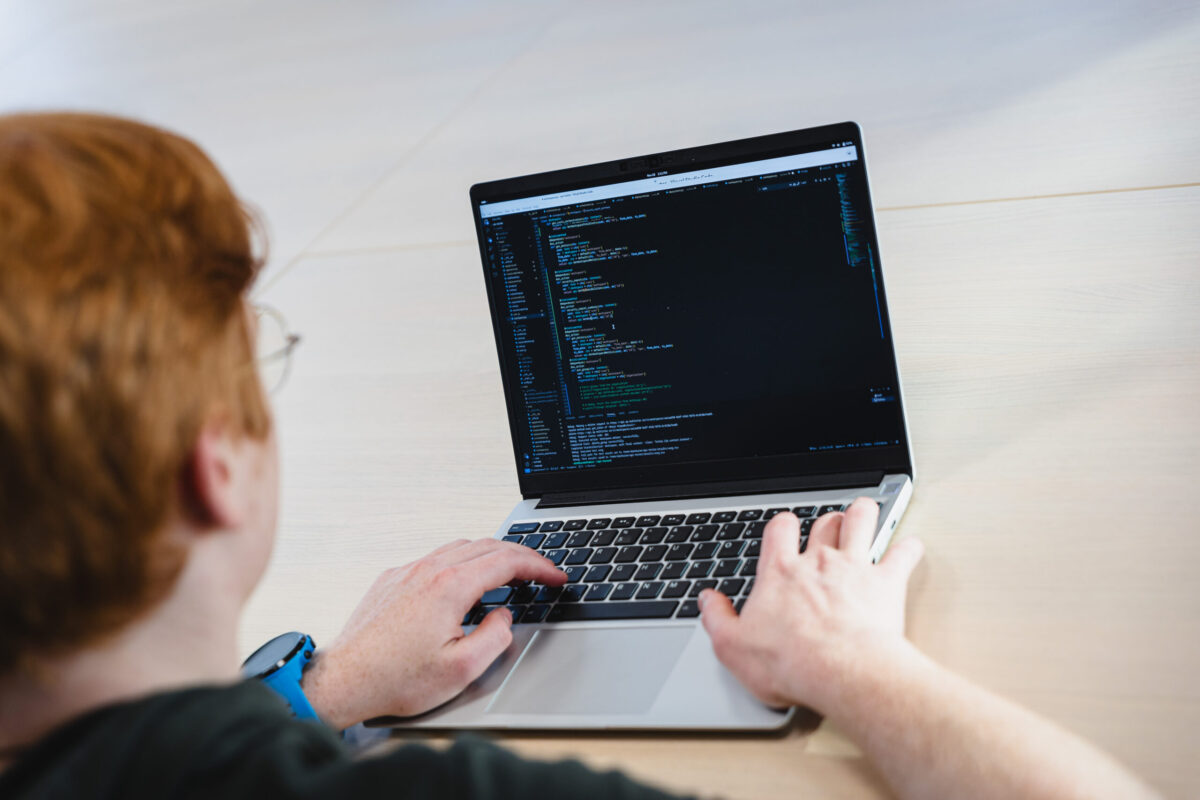 Person behind a laptop seen from behind. Lines of code on the screen.