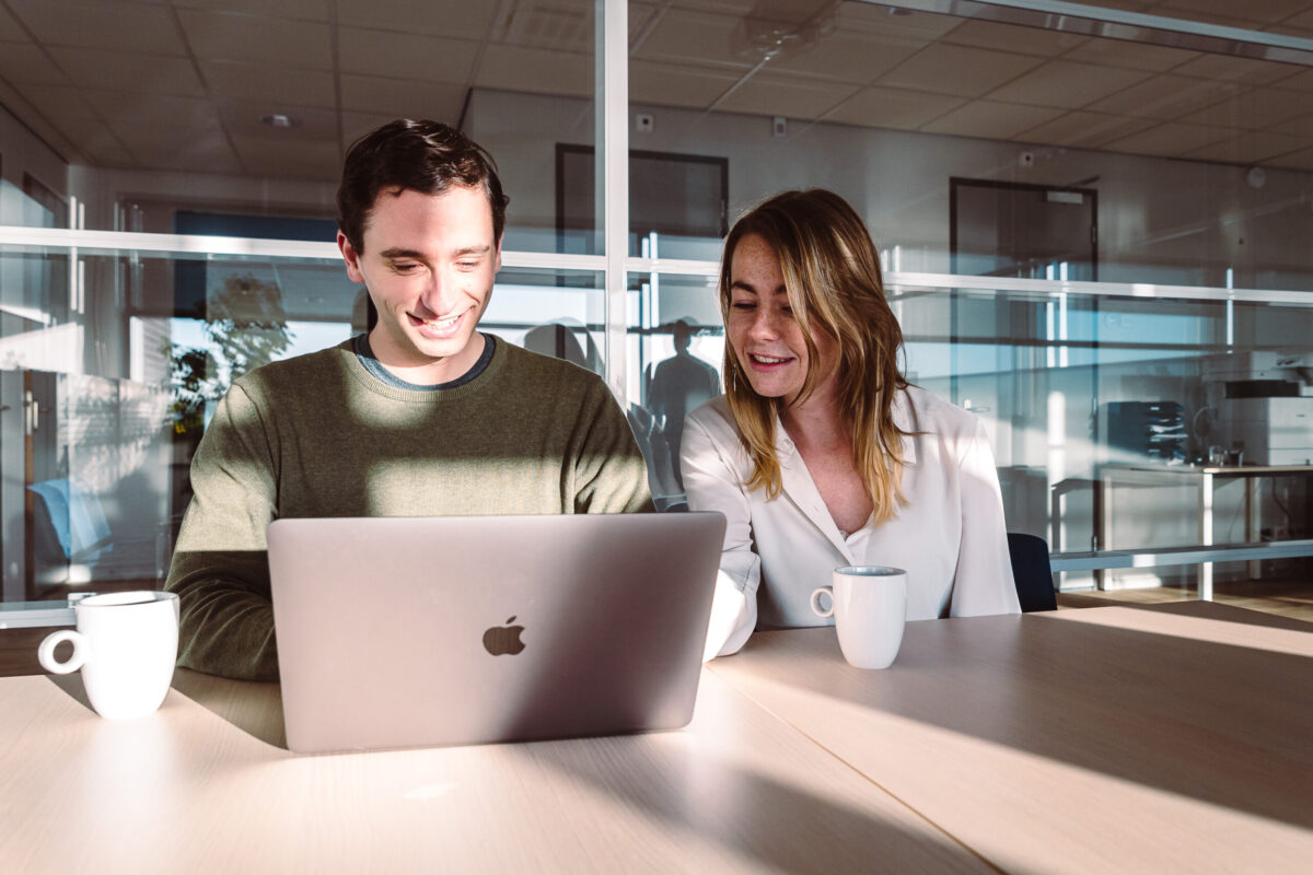 Two people sitting next to each other behind a laptop.