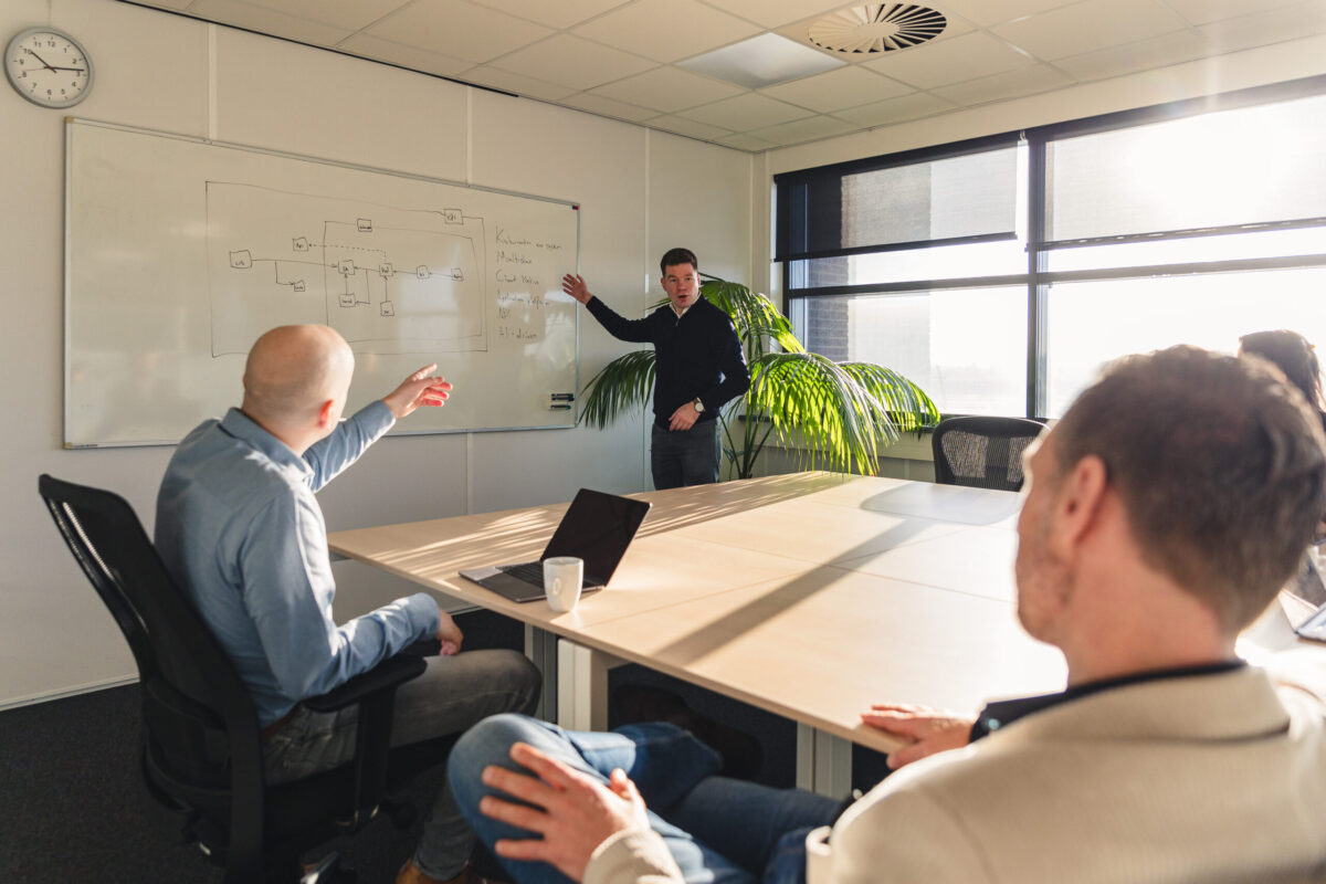 Three people in a meeting room. One person standing in front of a whiteboard.