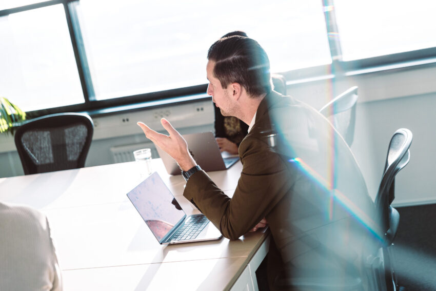 People in a meeting room with a laptop on the table, seen trough glass.